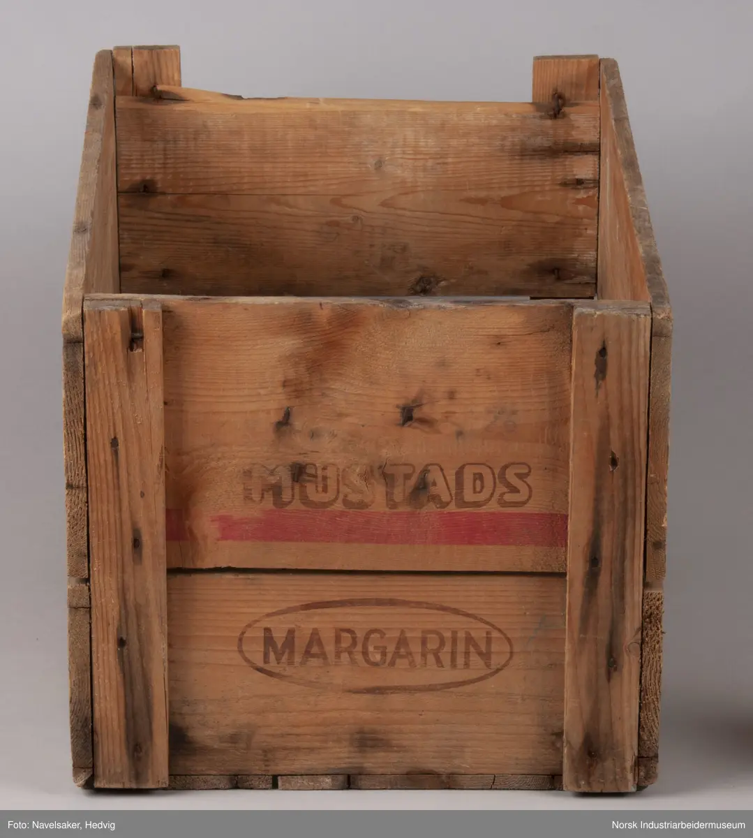Trekasse fra O. Mustad & Søn for margarin. Kassen består av to plank på hver side. I kortsiden er plankene festet 1,5 cm på innsiden av plankene på langisden. Plankene er festet i hvert hjørne via en vertikal planke med spiker.