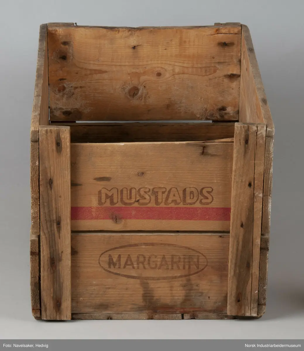 Trekasse fra O. Mustad & Søn for margarin. Kassen består av to plank på hver side. I kortsiden er plankene festet 1,5 cm på innsiden av plankene på langisden. Plankene er festet i hvert hjørne via en vertikal planke med spiker.
