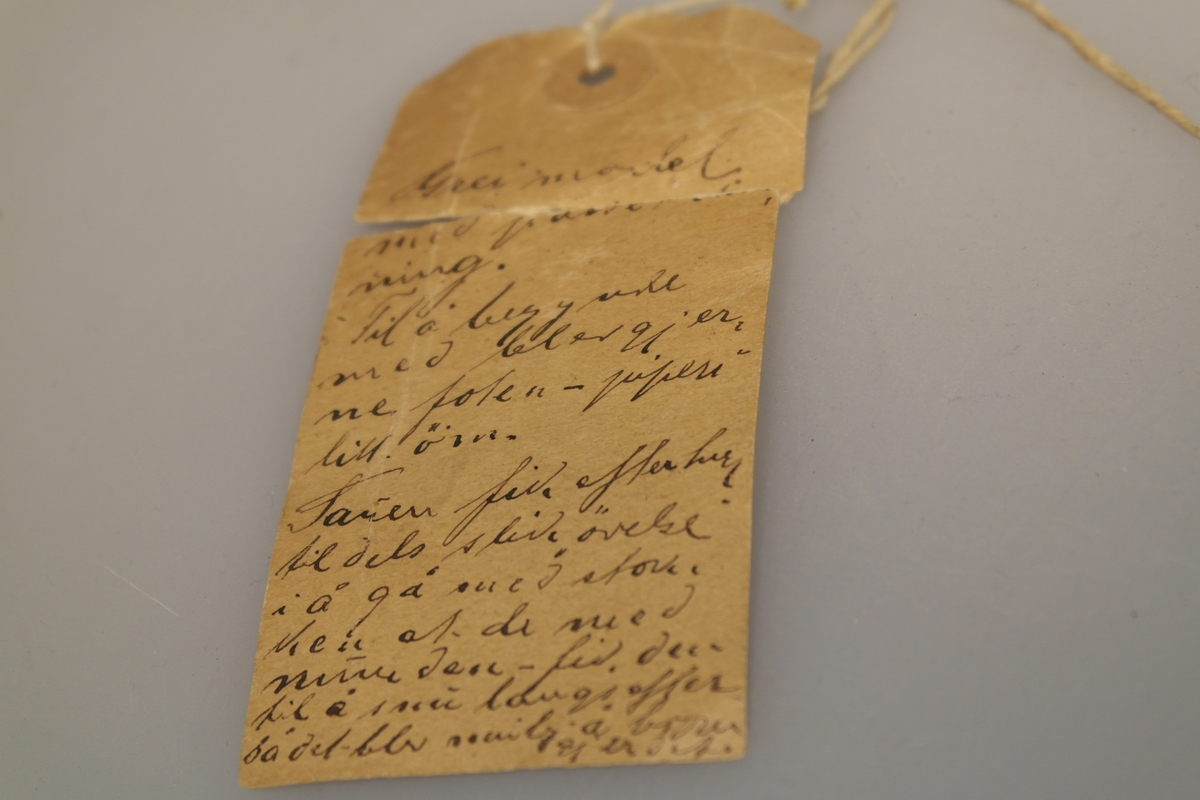 Sauestokk i tre. Stokken er buet og har en rund utsparing på midten samt to små hull på hver side av utsparingen. På den ene siden er det inngravert ett kryss samt et håndskrevet personnavn. En merkelapp med håndskrevet tekst har vært festet til stokken med hyssing. Stokken ble brukt for å hindre sau å hoppe over gjerde o.l. ved å feste den til sauens ben.