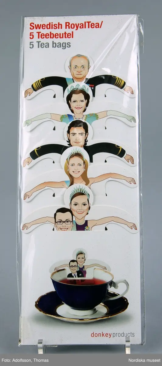 Tepåse, 5 st, i förpackning av transparent plast. Tepåsar i form av illustrationer av kungafamiljen,  Figurernas överdelar är utformade med utsträckta armar så att de kan hängas på tekoppens kant. motiven är: H. M. Konung Carl XVI Gustav, H.M. Drottning Silvia, H. K. H. Prins Carl-Philip, H. K. H. Prinsessan Madelen, H. K. H. Kronprinsessan Victoria och tillsammans med kronprinsessan H. K. H. Prins Daniel. Prins Daniel framstår som sittande i kronprinsessan Victorias knä. 

Text på framsidan: "Swedish RoyalTea/5 Teebeutel 5 Tea bags", "donkey produkts", 
Text på baksidan:"Swedish RoyalTea/5 Teebeutel 5 Tea bags", "We would like to share the enjoyment of this product. Therefore we are going to donate a part of the proceeds to Bethanien-Kinderdörfer. Assembled amongst others by: Elbe-Werkstätten GmbH, sheltered workshop." (också på tyska), "Classic tea blend with Assam, 5 individual tea bags Boiling water in a cup with a tea bag inside, leav to steep for 3-5 minutes." (också på tyska) "5 x 1,0 g = 5g Kühl & trocken lagern/Store in a cool and dry place MHD/Best before: 0212 "Dokey Products GmbH & Co. KG 20259 Hamburg, Germany", "Illustration: Thomas Kappers, www.tkgestaltung.de" 
 På baksidan prislapp/ettiket med streckkod/EAN-kod och text "Tepåsar Swedishh Royal T. 95:-"
/Johanna Krumlinde 2011