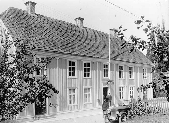 Hotell Brahe vid Brahegatan i Gränna. Vid entrén under skylten "Hotell Brahe" står vaktmästare Alfred Staf. På gatan står en Studebaker Big Six - cabriolet - med en man på väg in/ur bilen och intill en man klädd likt chaufför. Bilens registreringskylt säger P879.
