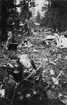 Haveridelar från flygplan B 3 Junkers Ju 86K i skogsparti. Flygplanet har slagits i småbitar och skapat en korridor mellan träden. Två personer står bredvid vrakresterna.