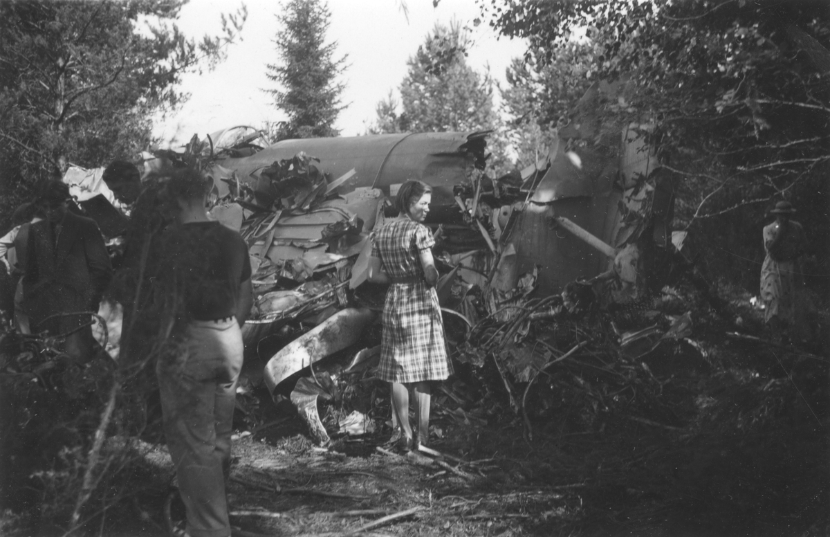 Haveridelar från flygplan B 3 Junkers Ju 86K i skogsparti. Flygplanet är kraftigt tilltyglat och har slagits i småbitar. Sex personer står vid vraket.