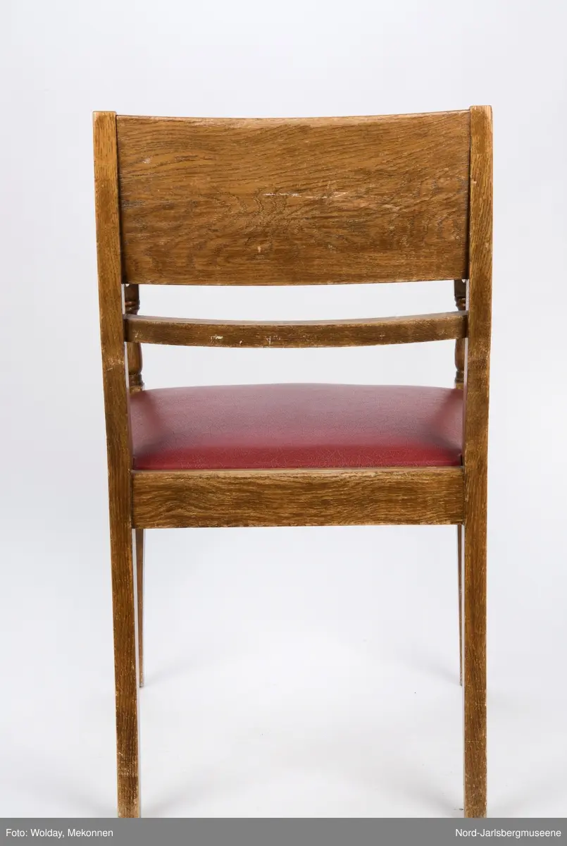 Stol i heltre med stoppet sete med rødt trekk. Stolen har forseggjorte armlener som avsluttes i en myk bue, med dreide detaljer. Ryggstø har en bred plate øverst og en tynnere list under den.