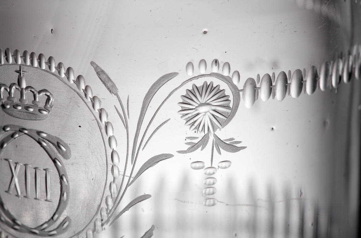 Dricksglas. Tillhör "Carl XIII:s servis".
Blåst 1810-1813. Graverat 1815-1818.
Graverat av Anders Spolander. Se E. Steenberg "Svenskt adertonhundratals glas", sidan 131,1).
Beskrivning: Cylindriskt. Monogram "C XIII" med krona, i en oval omgiven av stiliserade växter. Bård av små oliver och streck. Rad av ställda skär i mittpartiet. Facettslipad nederdel.
Färg: Ofärgat klarglas.
Teknik: Slipad kant. Planslipad botten med kula. Slipad och graverad dekor enligt ovan.
Märkning: Graverat nr. under foten. Se "Signering, märkning" ovan.
Inskrivet i huvudkatalogen tidigast 1976.

Enligt uppgift ägdes en del av servisen av Växjö regemente tills regementet upplöstes år 18??. Skänktes sedan till regementets officerare. Dessa pjäser tillhörde fänrik ....

Gravör Anders Spolander, född i Umeå den 27 juli 1782, arbetade som glassliparlärling vid Strömbäcks glasbruk 1806-1812, vid Kungsholms glasbruk 1812-1813, och 1813 vid en egen verkstad för "glasritning". Dog 1836. Hans verkstad drevs av änkan till 1843.
Funktion: Dricksglas