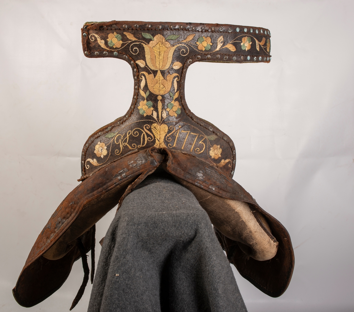 Brodert lær. Grønn mønstret  fløyel i setet og på armlene. Messinghode på fremre del av rygglenet. Initialene KDS og årstallet1773 brodert på. Løs narv på kappene, redrot.