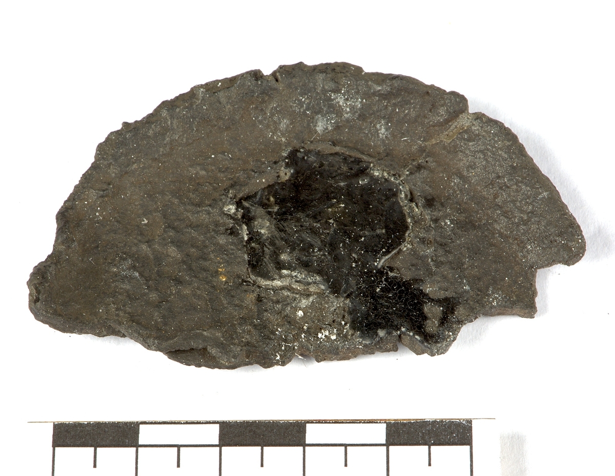 Ett fragment från ett oidentiferat föremål i järn bestående av en halvcirkelformad platta i järn.