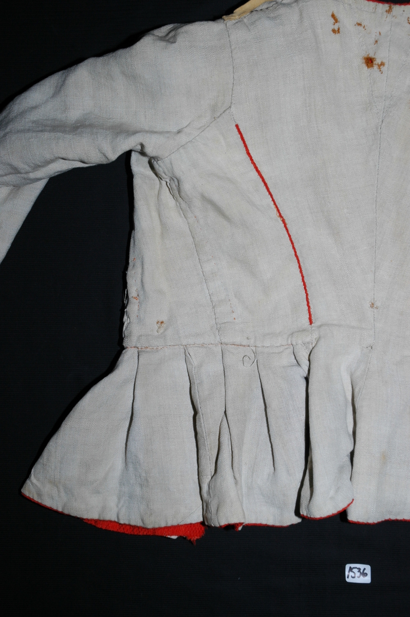 Trøye av rødt ullstoff med linfôr. Stoffet er av kamgarn og ble antageligvis solgt under betegnelsen everlasting på 1700-tallet. Produksjonssted er antageligvis England. Stoffet er i toskaft binding med flotteringer over tre tråder som gir mønstereffekt. Trøya har vært lukket med ni hekter og maljer midt framme. Snitt: Framstykkene er avdelt i midjen med kappe. Ryggstykkene går helt ned i skjøten. Kappa er foldelagt med sju folder (fra 10 cm midt framme). Foldene er 3-3,5 cm brede og 1,5 cm dype. Bua ryggsømmer sydd med spilesøm. Ryggsømmen midt bak er sydd med attersting hver for seg, men festet sammen i fôr og hovedstoff på noen steder. Det er to innsnitt under hvert herme. Ytterkantene er faldet med faldeprikkesting. Det er ekstra prikkestingsrad ved halsringing (1 cm fra ytterkant) og ved hektestillinga omlag 2 cm fra ytterkanten framme. Kappa er sydd til bolen med attersting (tre lag stoff). Fôret i bolen er bretta og lagt til og sydd ned i fôret til kappa. Kappa skrår bakover midt framme. Trange ermer sydd sammen med attersting. Sømmonnet er lagt mot bolen og fôret i bolen er lagt mot ermet og sydd til med faldesting. Skinnhemper til opphenging. Ensømserme med albuestnitt. På unerermene er det et innsnitt. Underermssømmer er sydd med attersting, stoff og fôr hver for seg (festet sammen på enkelte steder). Innsnittene er sydd med stoff og fôr sammen og lagt til en side og stukket ned, faldet til side. (Fra regsitrering ved Bunad- og folkedraktrådet/Norsk institutt for bunad og folkedrakt v/Jon Fredrik Skauge i 2005, revidert v/Bjørn Sverre Hol Haugen 2020). 