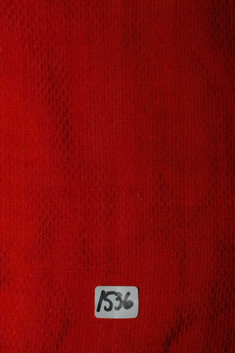 Trøye av rødt ullstoff med linfôr. Stoffet er av kamgarn og ble antageligvis solgt under betegnelsen everlasting på 1700-tallet. Produksjonssted er antageligvis England. Stoffet er i toskaft binding med flotteringer over tre tråder som gir mønstereffekt. Trøya har vært lukket med ni hekter og maljer midt framme. Snitt: Framstykkene er avdelt i midjen med kappe. Ryggstykkene går helt ned i skjøten. Kappa er foldelagt med sju folder (fra 10 cm midt framme). Foldene er 3-3,5 cm brede og 1,5 cm dype. Bua ryggsømmer sydd med spilesøm. Ryggsømmen midt bak er sydd med attersting hver for seg, men festet sammen i fôr og hovedstoff på noen steder. Det er to innsnitt under hvert herme. Ytterkantene er faldet med faldeprikkesting. Det er ekstra prikkestingsrad ved halsringing (1 cm fra ytterkant) og ved hektestillinga omlag 2 cm fra ytterkanten framme. Kappa er sydd til bolen med attersting (tre lag stoff). Fôret i bolen er bretta og lagt til og sydd ned i fôret til kappa. Kappa skrår bakover midt framme. Trange ermer sydd sammen med attersting. Sømmonnet er lagt mot bolen og fôret i bolen er lagt mot ermet og sydd til med faldesting. Skinnhemper til opphenging. Ensømserme med albuestnitt. På unerermene er det et innsnitt. Underermssømmer er sydd med attersting, stoff og fôr hver for seg (festet sammen på enkelte steder). Innsnittene er sydd med stoff og fôr sammen og lagt til en side og stukket ned, faldet til side. (Fra regsitrering ved Bunad- og folkedraktrådet/Norsk institutt for bunad og folkedrakt v/Jon Fredrik Skauge i 2005, revidert v/Bjørn Sverre Hol Haugen 2020). 