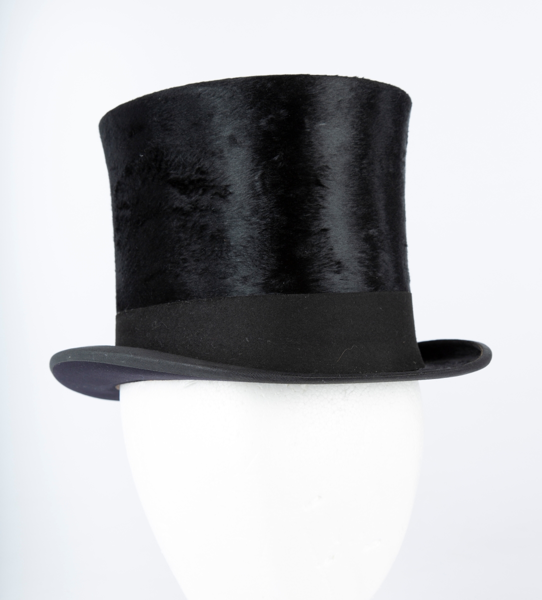 Oval hatt, rett pull med flat topp, flosset stoff, matt hattebånd. Flar brem forran og bak, oppbøyet sidekant. Foret med brun ripssilke. Svettekant i skinn.
Inni hatten et visittkort  med påskrift J. Schaan Theiste, Burauchef

 største LlxB: 30x24  Innvendig mål: L 20  B 15  H 15