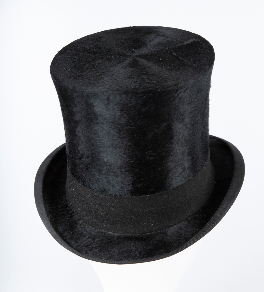 Oval hatt, rett pull med flat topp, flosset stoff, matt hattebånd. Flar brem forran og bak, oppbøyet sidekant. Foret med brun ripssilke. Svettekant i skinn.
Inni hatten et visittkort  med påskrift J. Schaan Theiste, Burauchef

 største LlxB: 30x24  Innvendig mål: L 20  B 15  H 15