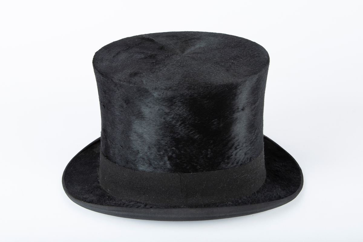 Oval hatt, rett pull med flat topp, flosset stoff, matt hattebånd. Flar brem forran og bak, oppbøyet sidekant. Foret med brun ripssilke. Svettekant i skinn.
Inni hatten et visittkort  med påskrift J. Schaan Theiste, Burauchef

 største LlxB: 30x24  Innvendig mål: L 20  B 15  H 15