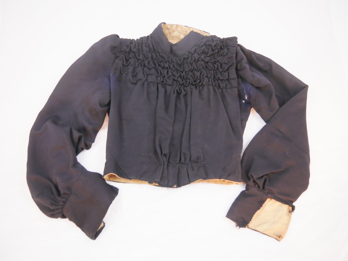 Kort overdel som høyrer saman med skjørt til kjole ("bykjole").
Har høg halslinning, ermene er rynka ved skuldrane og har breie ermkragar. Lukkinga er på venstre sida, slik at framstykket blir heilt. Dette er rynka i fleire felt med dekorativ verknad. Foret har lukking mist framme med ti sett hekter og hemper, det eine manglar.