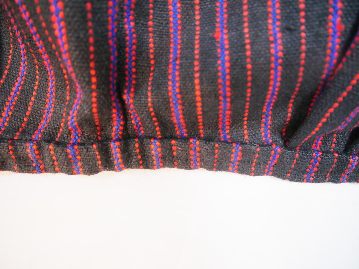 Forkle, randa. Også reg. som L.nr. 1987-102. vove i to lengder som er sydd saman midt framme med maskinsaum. Smal fald nede sydd med maskin. Linning av forklestoffet. To folder framovervende og to bakovervende på kvar side av eit glatt midtparti. Krok i kvar side av linningen