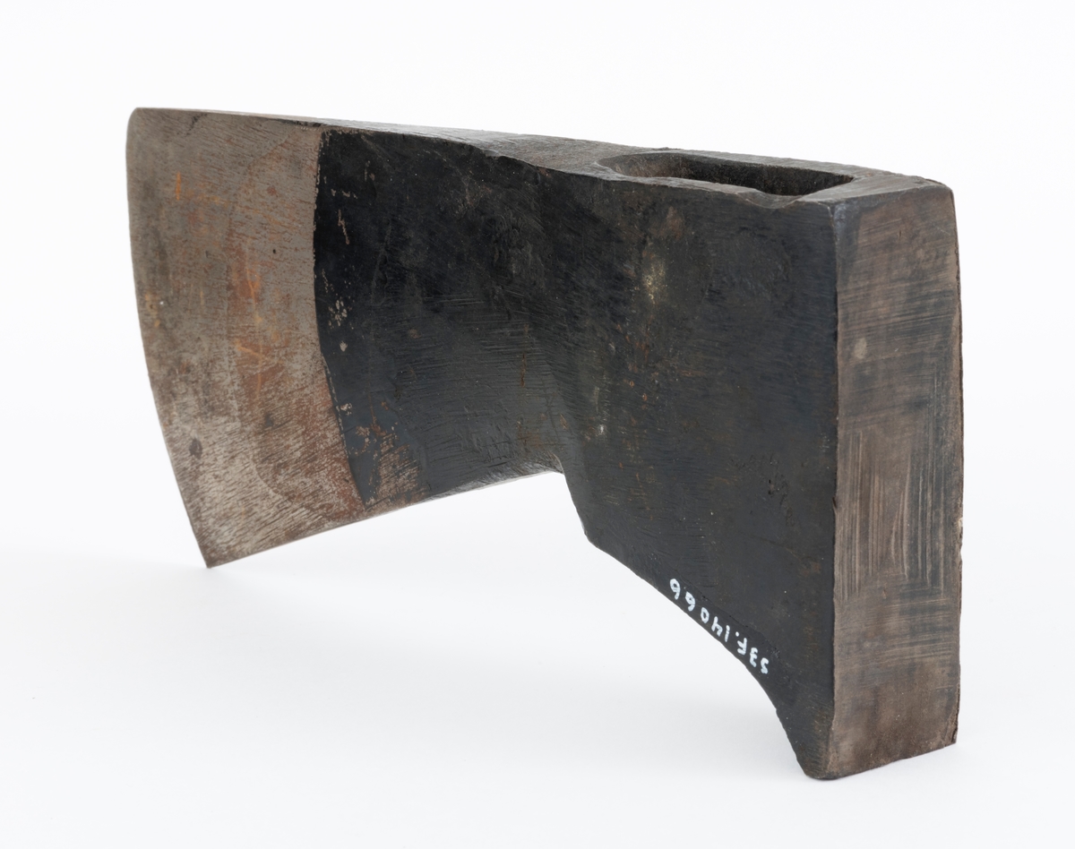 Uskjeftet øks fra produsenten O. Mustad & Søn på Gjøvik i Oppland. Øksehodet er 21,1 centimeter høyt, målt vinkelrett fra midten av den noenlunde plane nakkeflata ned mot den fremre delen av egglinja. Den nederste delen av øksebladet er 9,0 centimeter bred. Her er målet tatt i rett linje mellom den konvekse eggens ytterkanter. Den fremre tverrenden på øksehodet er noenlunde rettlinjet. På «baksida» skrår bladet noe innover mot et punkt like under «øyet» (skafthullet), der bredden er 5,7 centimeter. På denne sida øker bredden på «kjakene» mot den bakre enden av nakkepartiet. Hammerflata på denne delen av øksa er 9,6 centimeter langt og om lag 3,1 centimeter bredt bakerst, 2,8 i den fremre enden. På den høyre sida av øksenakken (sett i øksebrukerens perspektiv) finnes et svakt preget ovalt stempel med teksten «MUSTAD ØKS». Den øvre delen av øksehodet er svartlakkert, mens ei cirka 5,5 centimeter bred sone nederst på bladet er stålblank.