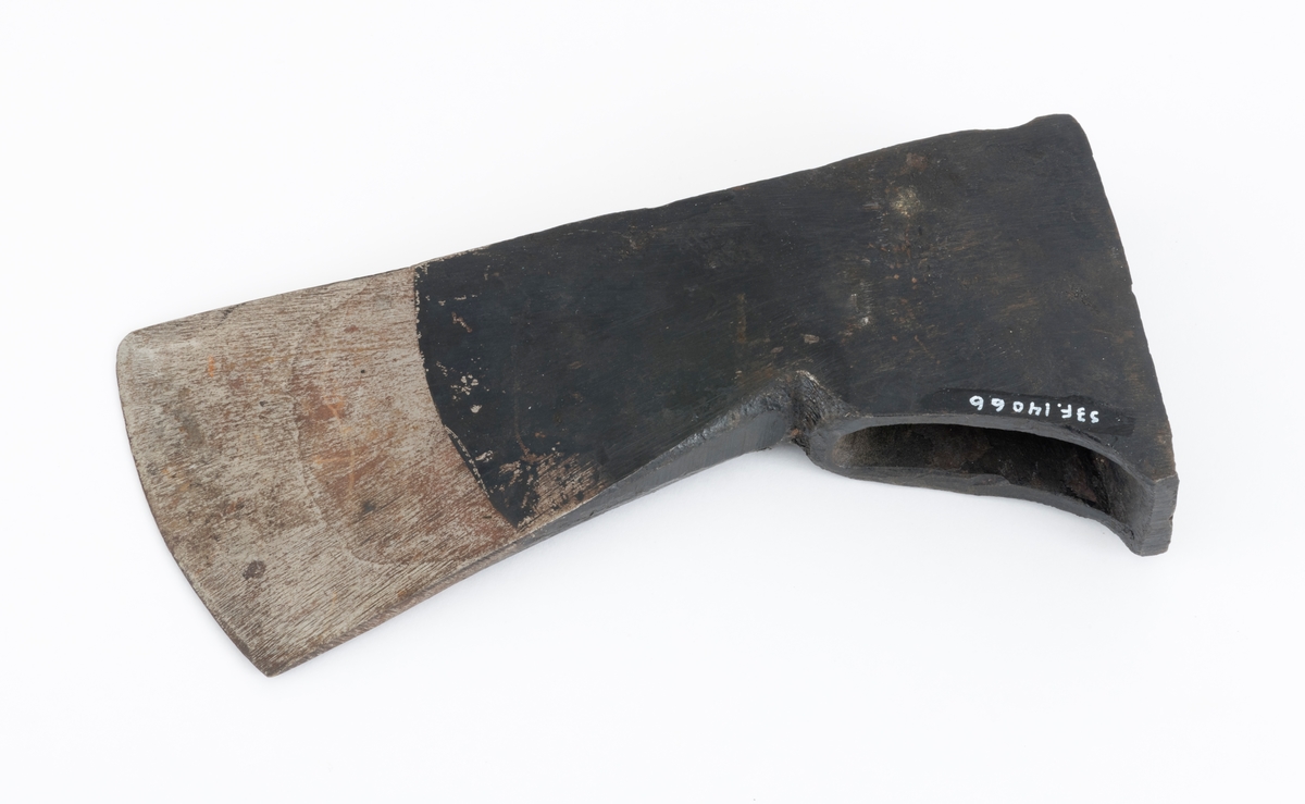 Uskjeftet øks fra produsenten O. Mustad & Søn på Gjøvik i Oppland. Øksehodet er 21,1 centimeter høyt, målt vinkelrett fra midten av den noenlunde plane nakkeflata ned mot den fremre delen av egglinja. Den nederste delen av øksebladet er 9,0 centimeter bred. Her er målet tatt i rett linje mellom den konvekse eggens ytterkanter. Den fremre tverrenden på øksehodet er noenlunde rettlinjet. På «baksida» skrår bladet noe innover mot et punkt like under «øyet» (skafthullet), der bredden er 5,7 centimeter. På denne sida øker bredden på «kjakene» mot den bakre enden av nakkepartiet. Hammerflata på denne delen av øksa er 9,6 centimeter langt og om lag 3,1 centimeter bredt bakerst, 2,8 i den fremre enden. På den høyre sida av øksenakken (sett i øksebrukerens perspektiv) finnes et svakt preget ovalt stempel med teksten «MUSTAD ØKS». Den øvre delen av øksehodet er svartlakkert, mens ei cirka 5,5 centimeter bred sone nederst på bladet er stålblank.