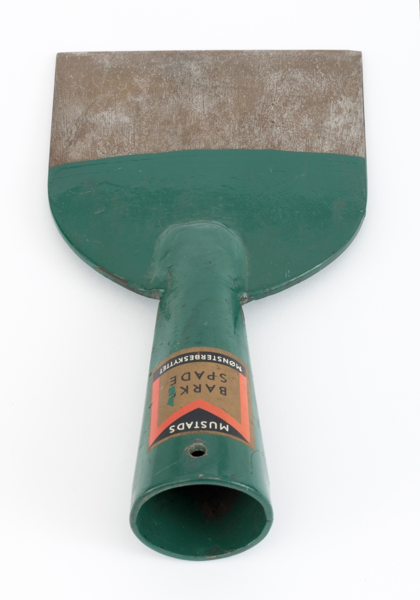 Barkespade fra O. Mustads fabrikker. Barkespaden består av ei plan stålplate med ei påsveiset, kon stålhylse i forlengelsen av bladets midtakse, i overenden.  Bladet er 12 centimeter bredt ved eggen, og egglinja er ubetydelig konvekst buet.  Den øvre enden av bladet var derimot tydelig buet, nærmest halvsirkelformet.  Her er bladet drøyt 4 millimeter tjukt.  Falen er lagd av 3 millimeter tjukt stål.  Den er tilpasset en kjegleformet skaftende og har et gjennombrutt hull med cirka 5 millimeters diameter, antakelig for en skrue eller spiker som skulle forebygge at stålet løsnet fra treskaftet.  Den øvre delen av bladet og falen er innsatt med mørkegrønn lakk.  På falens ytterside er det påsatt en rektangulær etikett med en rød «M» for Mustad på gullfarget og svart botn.  På den samme etiketten finner vi teksten «MUSTADS BARKESPADE MØNSTERBESKYTTET».  Denne barkespaden har ingen nevneverdige slitasjespor som kan tyde på at den har vært brukt i skogen, og den har sannsynligvis aldri vært skjeftet.