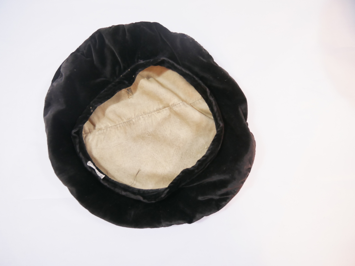 Hovudplagg av  "alpehuetype" med flat, rund pull og linning rundt hovudet. Det er mogleg det her skal vere band eller anna dekor. Fôra med ubleika bomull.