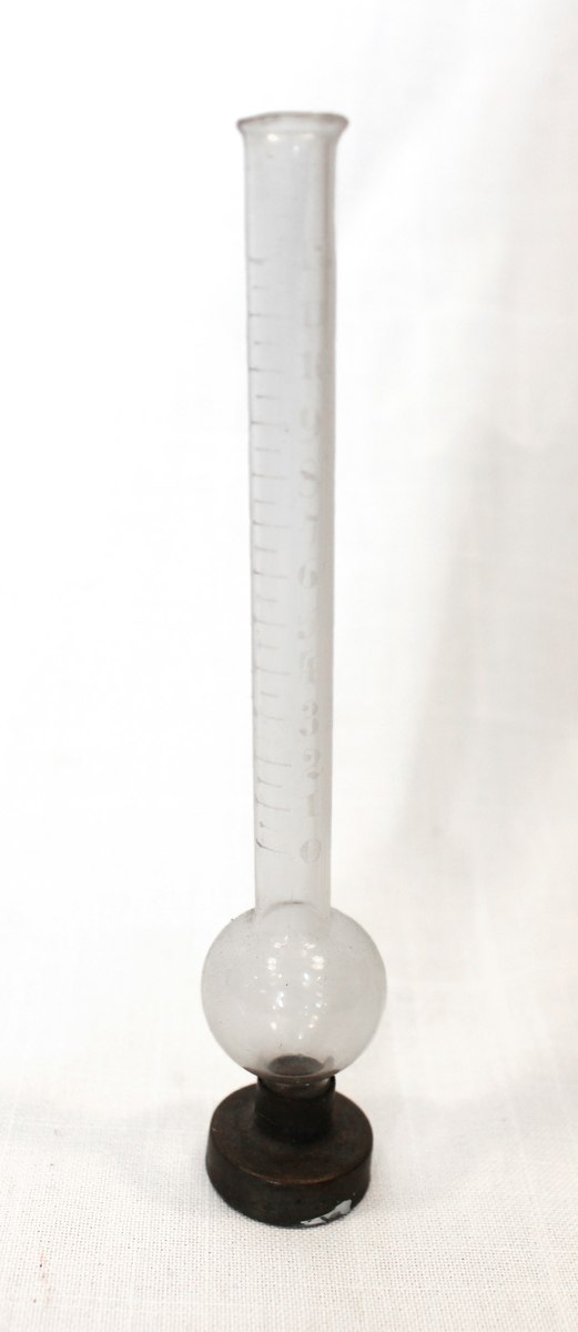 Målekolbe med graderinger, fra 0 til 12, i glasset. Foten er av kobber.