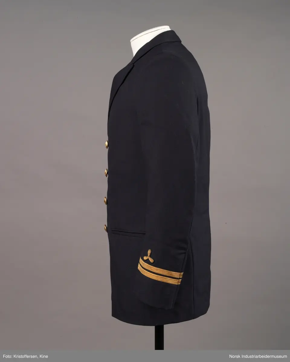 Uniformsjakke til maskinist med åtte gullknapper med ankerlogo. To striper og propellogo i gull på hvert erme.