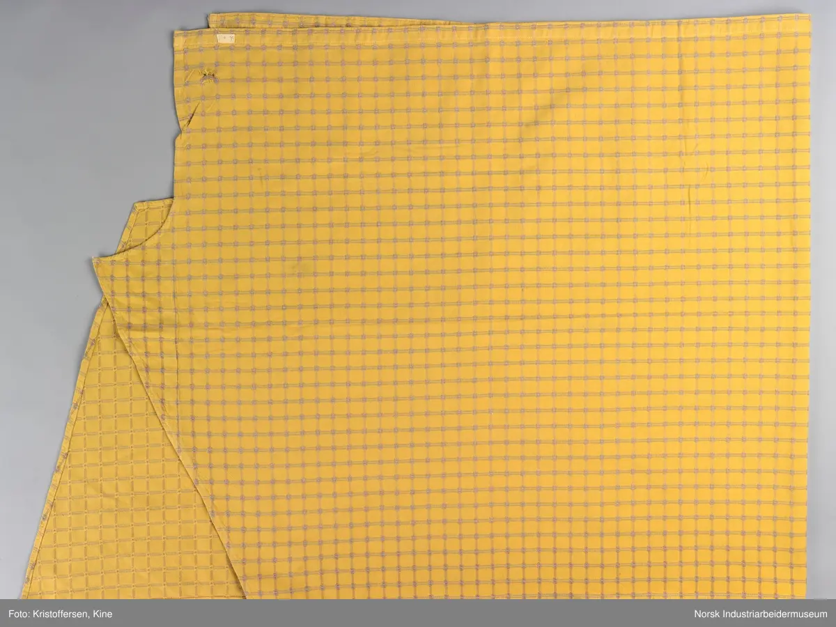 Gult stoffstykke satt sammen av tre stykker. Det er skjøtet 37 cm. fra høyre kant oppe. Pen skjøt, følger mønsteret. Jarekantene er ikke klippet av, men ligger på baksiden som sømningsmonn. På den andre siden, venstre side, er det satt på et lite stoffstykke ekstra. Det er gjort på samme måte, altså med en pen skjøt der mønsteret stemmer. Det er smale falder rundt hele stykket, men i overkant er den litt bredere. Det er et hull i stoffet. Stoffet er generelt ikke veldig slitt, og det virker ikke som dette hullet er forårsaket av alminnelig slitasje. Det må snarere være resultat av en spesiell påvirkning på akkurat det stedet. Pålimt lapp: F 09.