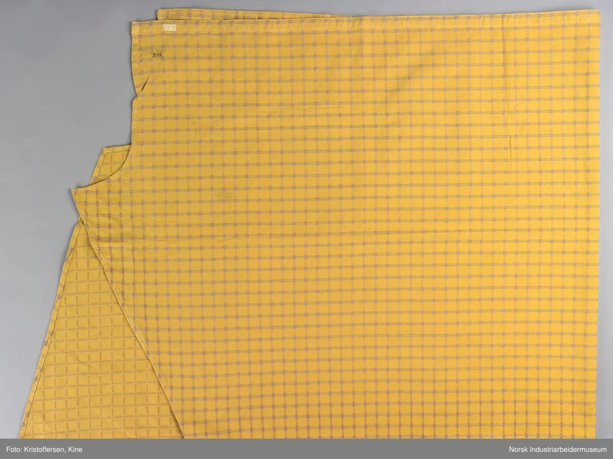 Gult stoffstykke satt sammen av tre stykker. Det er skjøtet 37 cm. fra høyre kant oppe. Pen skjøt, følger mønsteret. Jarekantene er ikke klippet av, men ligger på baksiden som sømningsmonn. På den andre siden, venstre side, er det satt på et lite stoffstykke ekstra. Det er gjort på samme måte, altså med en pen skjøt der mønsteret stemmer. Det er smale falder rundt hele stykket, men i overkant er den litt bredere. Det er et hull i stoffet. Stoffet er generelt ikke veldig slitt, og det virker ikke som dette hullet er forårsaket av alminnelig slitasje. Det må snarere være resultat av en spesiell påvirkning på akkurat det stedet. Pålimt lapp: F 09.