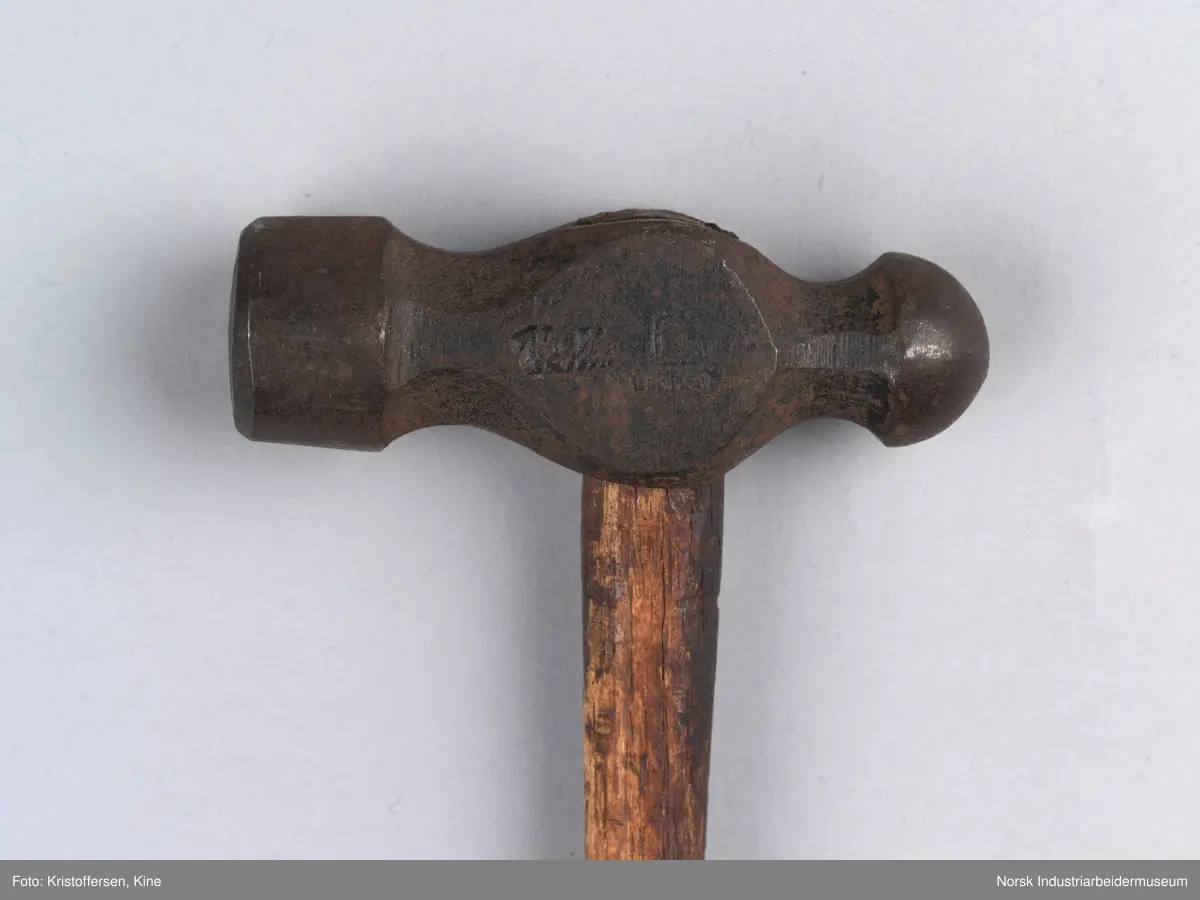 Vognvisitørhammer. Skaftet er 79 cm. langt. Skaftet er gjennomgående. Hodet er veldig svart og sitter litt slarkete. Merking: Lok. 9 er svidd inn. På hammerhodet står det: ½ lbs. Germany. Det er også et stempel i form av en stigbøyle