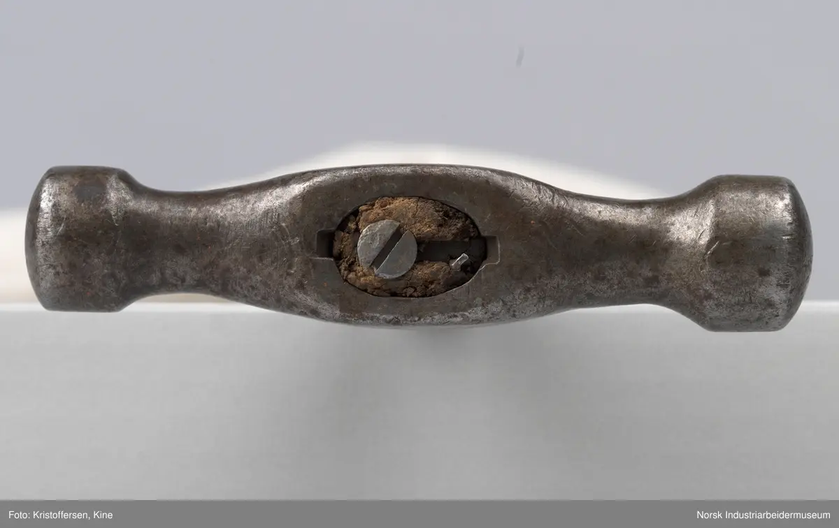 Vognvisitørhammer. Skaftet er gjennomgående. Hodet er blankslitt, metallisk av farge. Hodet har nok vært litt slarkete, for det er satt i en skrue i treverket i toppen for å utvide det slik at hammerhodet sitter godt på. Ingen stempler eller merker.