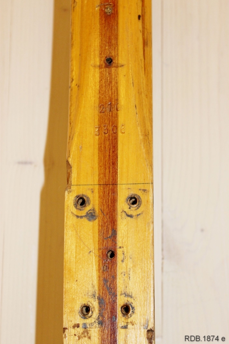 Avsmalende, jevnbred ski med liten bue. Bøy uten tupp. Rett avskåret bakende.
Dekorert med ei brun stripe på trehvit bunn.

Noen stempel fra OL øverst på skiet.