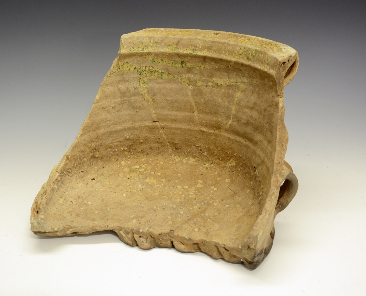 Fra protokollen: 
Keramikkskår. Tykt leirgods, flat bunn, utoverskrånende korpus som ender i en markert brutt kant oppe. Krukka har 4 dekorative ører nede på korpus og (1) og 2 større oppe. En mengde hull går inn i godset i bunnen og fra sidene av bunnen. Krukka mangler glasur, men har partivis (delvis) et slags grønnaktig belegg. Litt over halvparten av bunnen er bevart, men det meste av korpus er slått vekk. Krukka ble funnet i den under BM.1964:198, i merknadene, omtalte Bølebåten.