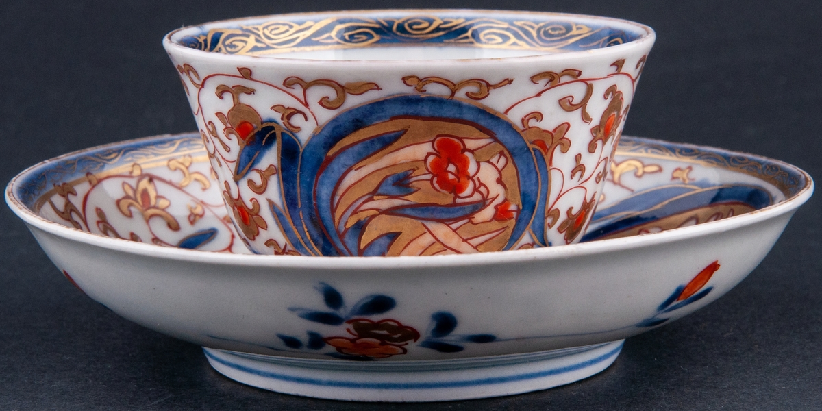 Kopp och fat, kopp utan öra. Vit glasyr med överglasyrmålning i blått, orange och guld. Utan stämpel, kompaniporslin.