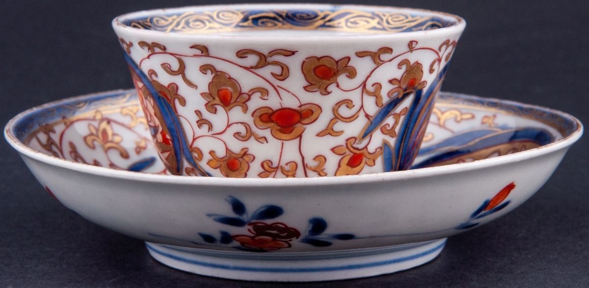 Kopp och fat, kopp utan öra. Vit glasyr med överglasyrmålning i blått, orange och guld. Utan stämpel, kompaniporslin.