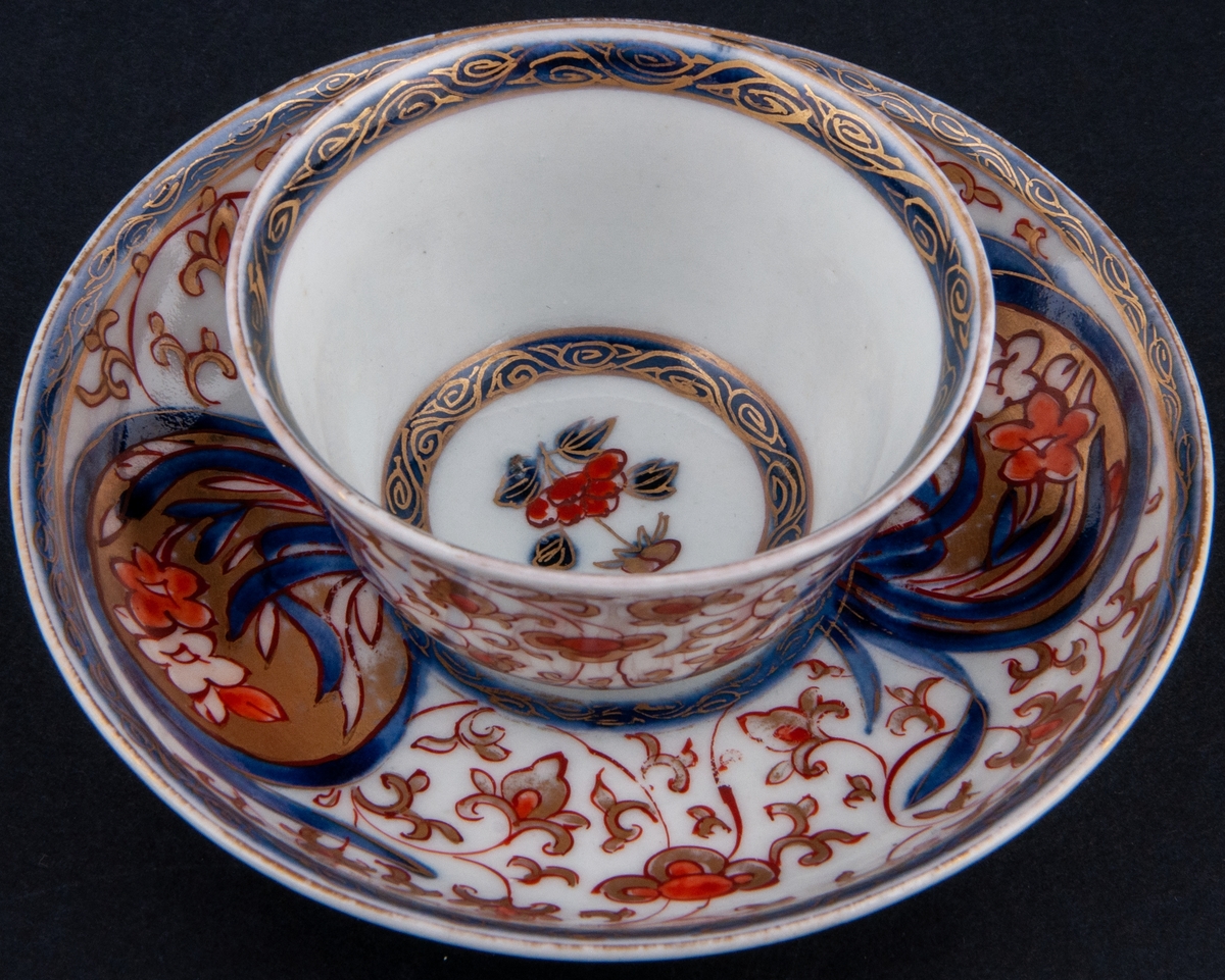 Kopp och fat, kopp utan öra. Vit glasyr med överglasyrmålning i blått, orange och guld. Utan stämpel, kompaniporslin.