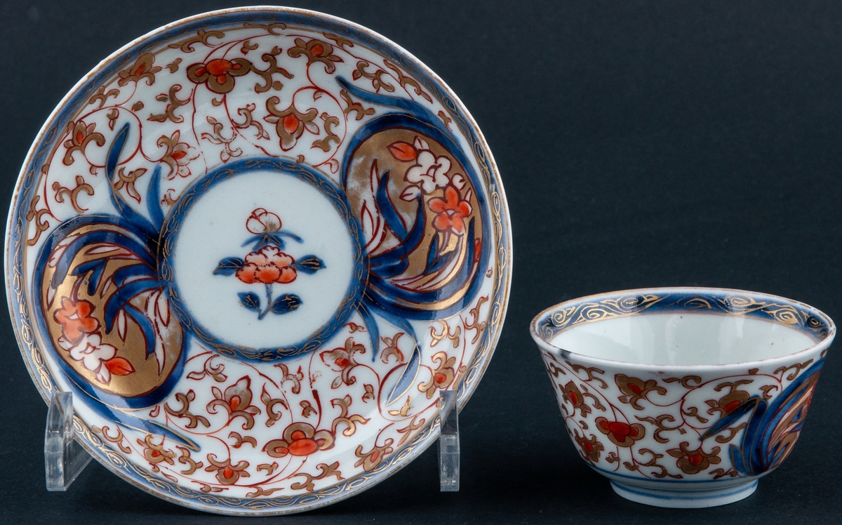 Kopp och fat, kopp utan öra. Vit glasyr med överglasyrmålning i blått, orange och guld. Utan stämpel, kompaniporslin.