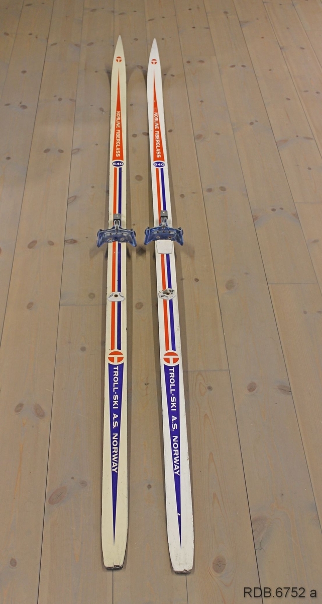 Et par Troll-ski, glassfiberski med trekjerne. Skiene er kvite med blå og røde dekorstriper og kvit påskrift. Skiene er jevnbrede men lett avfaset mot bakenden. Høg og spiss brett. Svarte sider og svart underside med ei egle. Påmontert blå Rottefellabindinger og kvit hælstøtte.