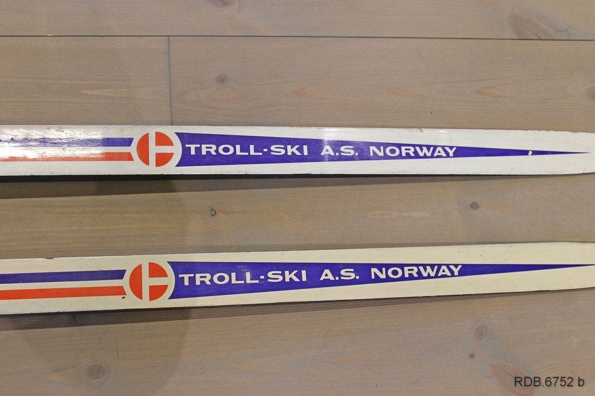 Et par Troll-ski, glassfiberski med trekjerne. Skiene er kvite med blå og røde dekorstriper og kvit påskrift. Skiene er jevnbrede men lett avfaset mot bakenden. Høg og spiss brett. Svarte sider og svart underside med ei egle. Påmontert blå Rottefellabindinger og kvit hælstøtte.