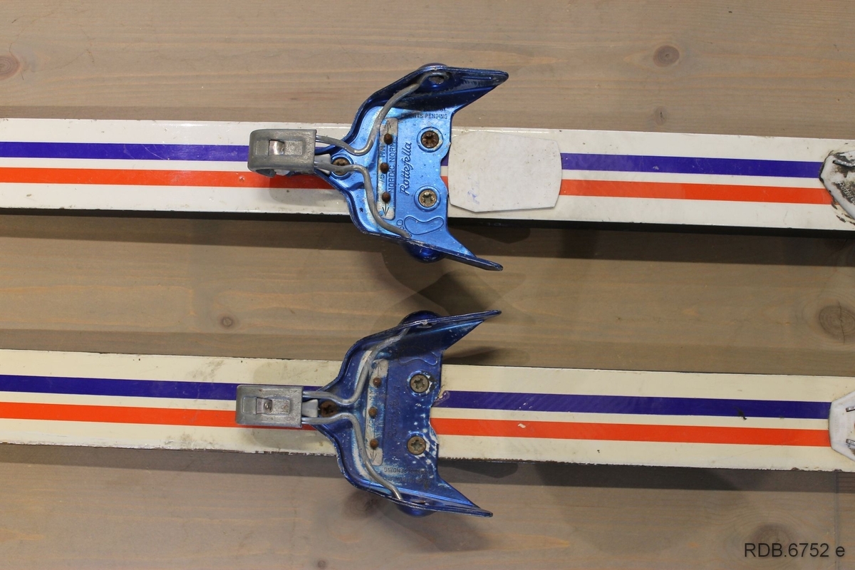 Et par Troll-ski, glassfiberski med trekjerne. Skiene er kvite med blå og røde dekorstriper og kvit påskrift. Skiene er jevnbrede men lett avfaset mot bakenden. Høg og spiss brett. Svarte sider og svart underside med ei egle. Påmontert blå Rottefellabindinger og kvit hælstøtte.