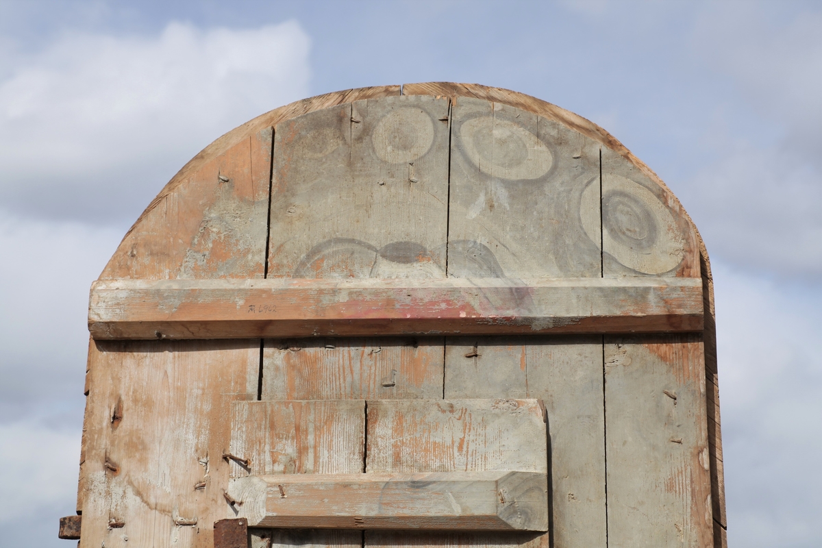 Døra er laget av 1 1/4 toms planker med to enkle drev som holder plankene sammen. Døra er belagt med profilert panel. Panelet er lagt på skrå i mønemønster og festet med spiker som har digre hoder. Døra har et vindu på 45 cm x 79 cm som innvendig er lukket med en liten hengslet dør. Døra er nærmest halvsirkelformet i toppen og passer da inn i buen i murverket. Låsen sitter på og har rombeformet nøkkelhullbeslag og to solide gangjern med to enkle knuter. Låsen sitter på innsida og er helt innebygd med jernplater og to slåtter. På innsida er rester etter påmalt marmorering.
