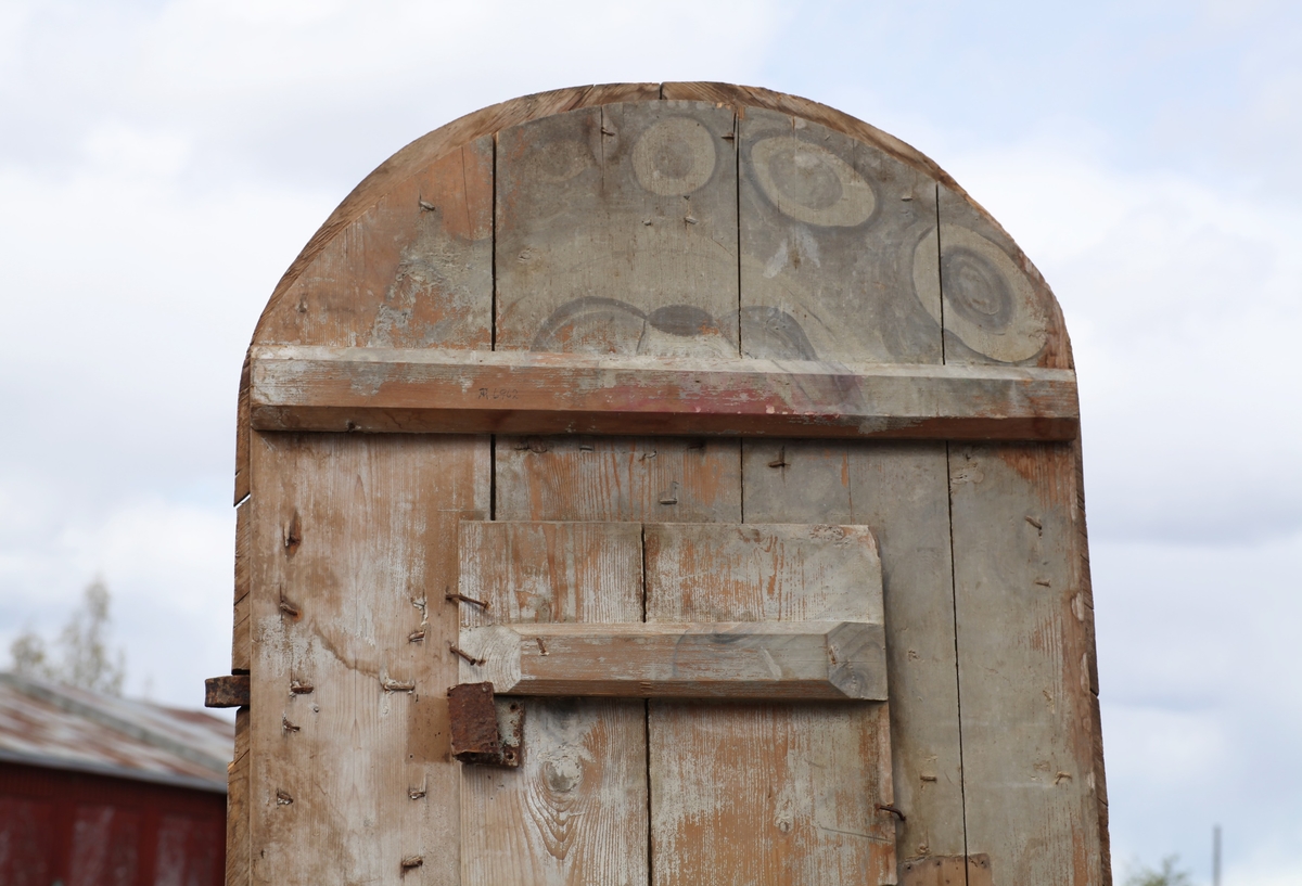 Døra er laget av 1 1/4 toms planker med to enkle drev som holder plankene sammen. Døra er belagt med profilert panel. Panelet er lagt på skrå i mønemønster og festet med spiker som har digre hoder. Døra har et vindu på 45 cm x 79 cm som innvendig er lukket med en liten hengslet dør. Døra er nærmest halvsirkelformet i toppen og passer da inn i buen i murverket. Låsen sitter på og har rombeformet nøkkelhullbeslag og to solide gangjern med to enkle knuter. Låsen sitter på innsida og er helt innebygd med jernplater og to slåtter. På innsida er rester etter påmalt marmorering.