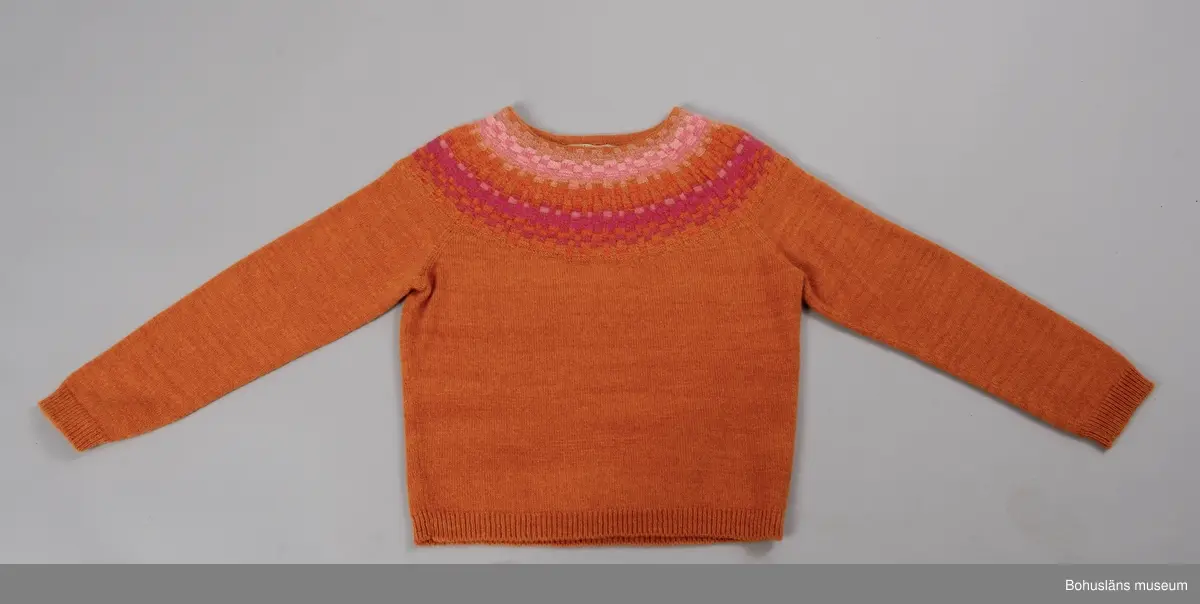 Nyproduktion av stickad jumper med lång ärm, stickad enligt "gamla rundstickningen". Oket är mönsterstickat med räta och aviga maskor i infärgade nyanser av orange och rosa, övriga partier slätstickade i orange. Dubbelvikt halsringning, på baksidan resårstickad. Resårstickade ärmmuddar och nederkant. Fastsydd etikett på insidan halsringningen med vävd text:
"BOHUSLÄNS MUSEUM efter original BOHUS STICKNING".