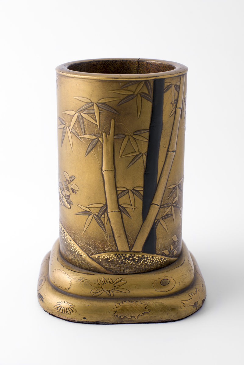 Rund vase av bambus (?) på avrundet, firkantet sokkel. Malt, lakkert eller glasert i relieff med motiv av bambus, blomster, hane, høne, orientalsk landskap.