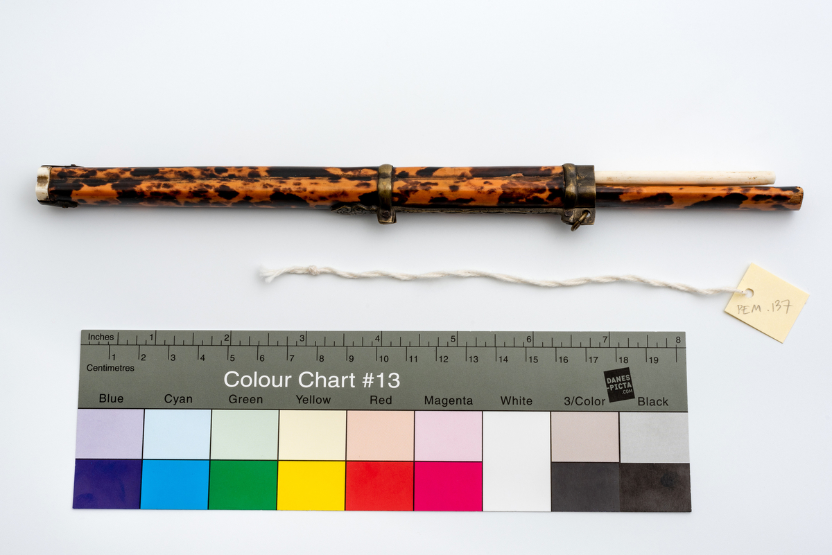 Kinesisk spisesett bestående av en slire i bambus dekket med skilpaddeskjell -finér med beinbunndeksel. 
I sliren en lang kniv med skaft i samme materiale som sliren og metallblad, og et sett (2 stk) spisepinner i bein.