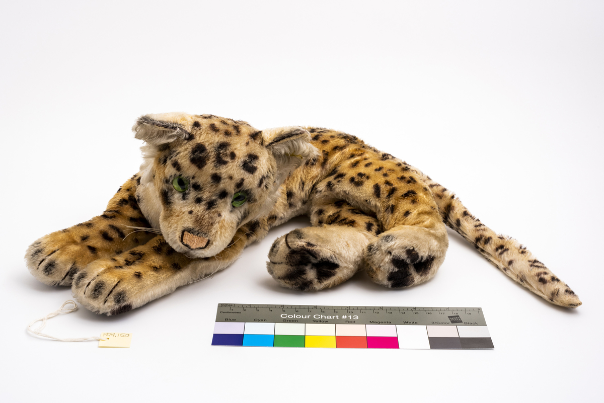Kosedyr. Forestiller liggende ozelot (kattedyr, ref. Steiff, nummer 2328). Påsydd snute, munn og tær på potene. Grønne glassøyne påsydd. Har tilhørt Sara Fabricius.