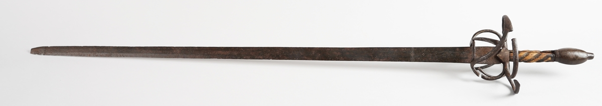 Kårde. Lang, rett klinge med tre kantar (på kvar side). Handtak i tre med spiralliner, solid jarnknapp nedst og metall handbeskyttelse. På kva side av klinga, ned mot handtaket, er det gravert tre kross eller stjerner, og innimellom første og andre stjerne, eit løpande dyr.