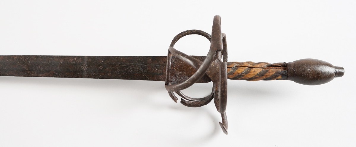 Kårde. Lang, rett klinge med tre kantar (på kvar side). Handtak i tre med spiralliner, solid jarnknapp nedst og metall handbeskyttelse. På kva side av klinga, ned mot handtaket, er det gravert tre kross eller stjerner, og innimellom første og andre stjerne, eit løpande dyr.