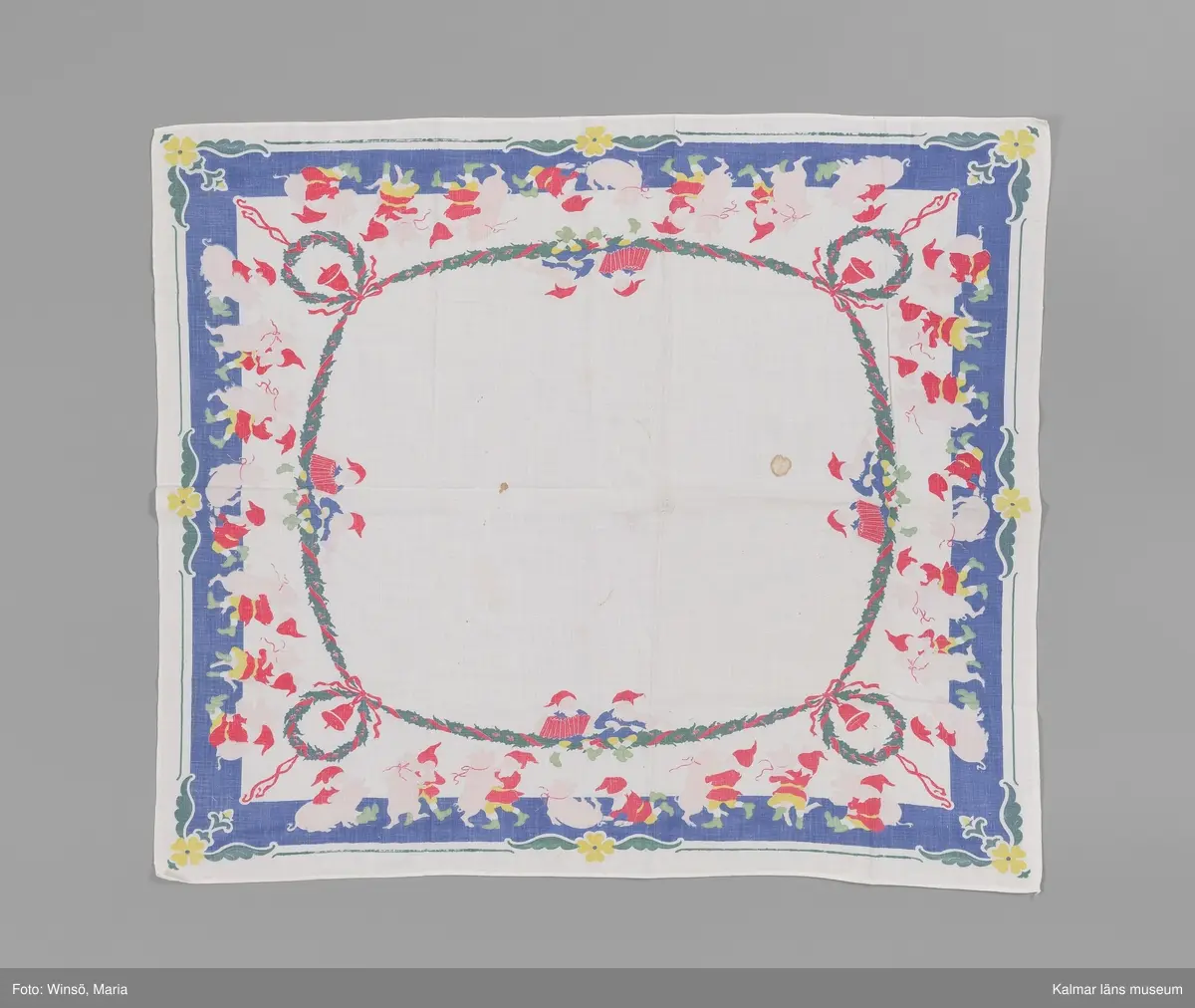 KLM 46157:674. Duk. Julduk. Av vit tuskaftad bomull. Kvadratisk. Tryckt bård längs kanterna i blått, rosa, rött, grönt och gult. Tomtar som dansar med grisar. Innanför bården granrisgirlang med röda band och tomtar som spelar dragspel och fiol. I hörn och mitt på sidorna gul blomma. Fållad i två sidor, de andra två stadkant. I ett av hörnen syns signaturen JN, för Jenny Nyström, svagt.
Duken är eventuellt blekt eller har den svarta färgen som ska vara tryckt som kontur till mönsterformerna inte blivit fixerad ordentligt. Den svarta färgen saknas nästan helt.