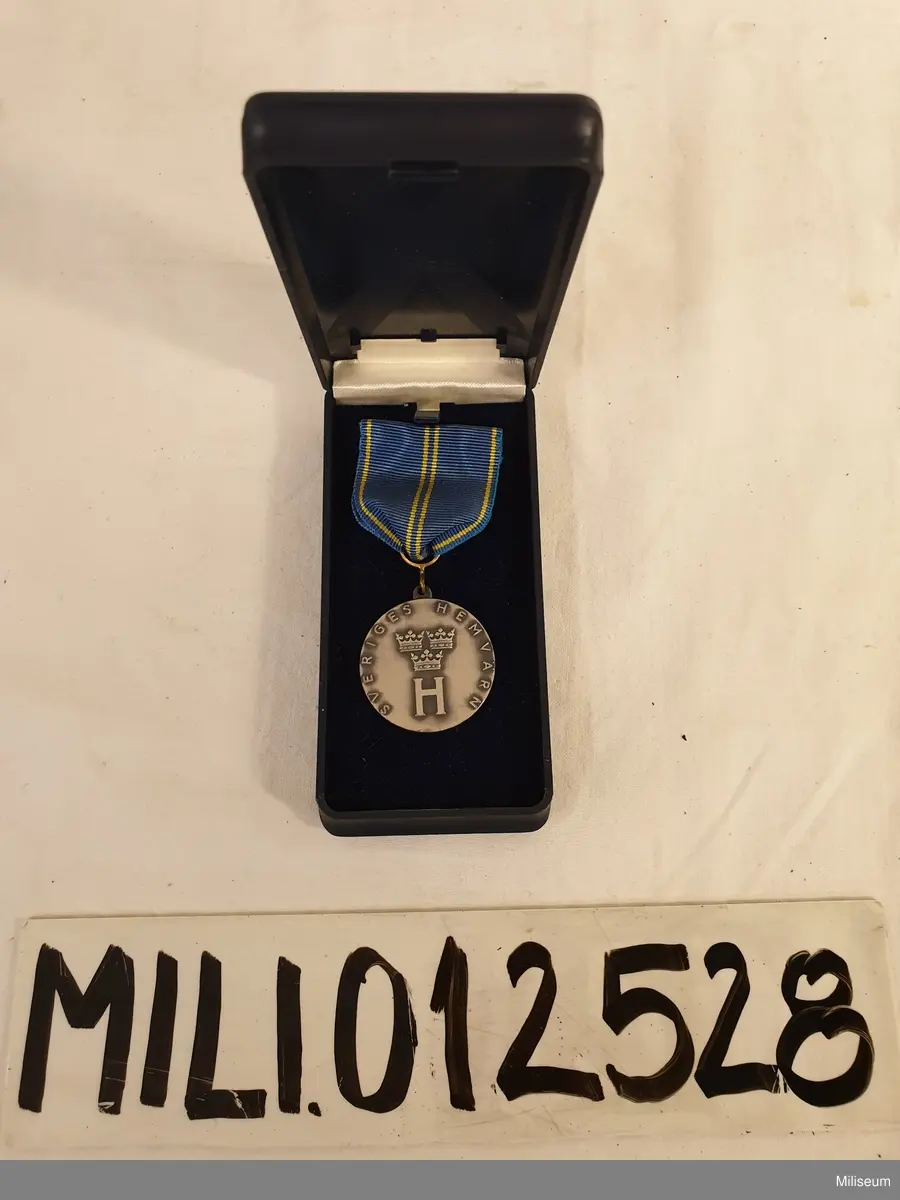 Hemvärnets förtjänstemedalj i valören silver, tillverkad av försilvrad mässing, med tillhörande etui av blå plast.