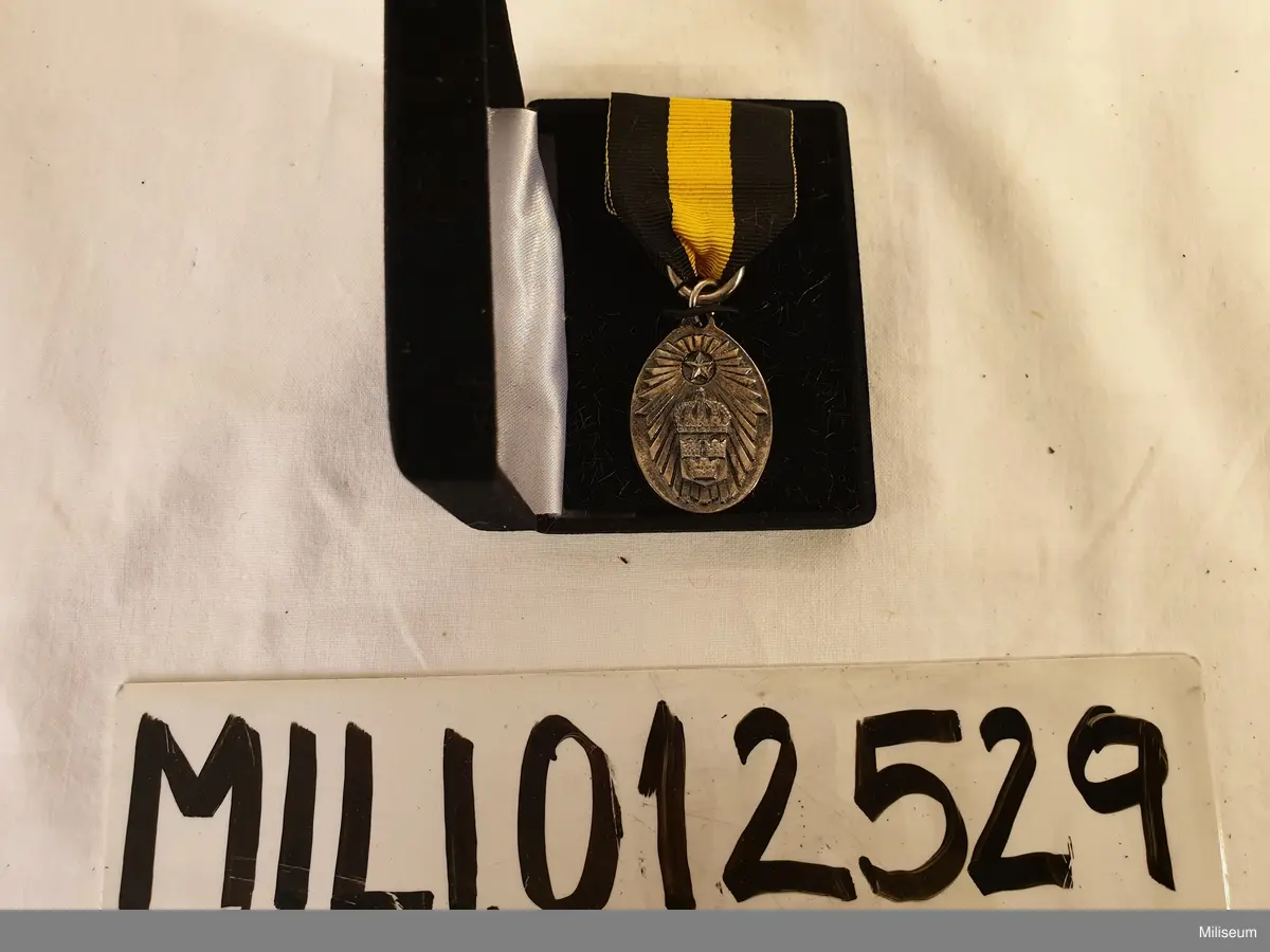 Hemvärnets förtjänstemedalj i valören silver, tillverkad av försilvrad mässing, med tillhörande bandspänne, extra ripsband och etui av svart plast.