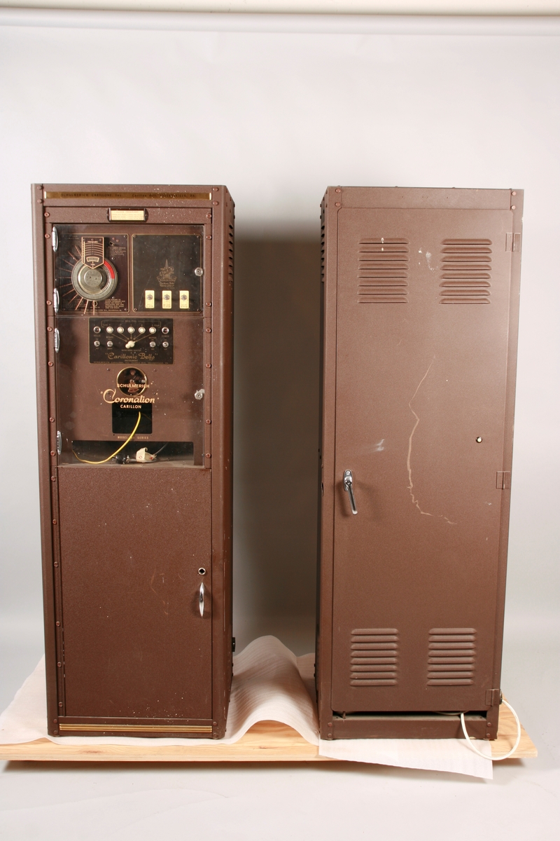 To brunmalte skap i metall (samme størrelse). Flere ventilasjonsrister.

Det ene skapet (A) inneholder avspiller, forsterker, klokkemekanikk, liten høytaler og øvrig elektronikk (noen deler ser ut å mangle). 
Øvre halvdel: bak pleksiglass som kan lukkes er styresentralen med instillinger for ulike klokkeprogrammer:
Til høyre er switch-knapper for å aktivere de tre funksjonene 
a) avspilling av musikkrull 
b) bruk av manuelt spillebord og 
c) timeslag.

Over til venstre er en timer for å skjemalegge de ulike aktivitetene:
1) Hverdag avspilling musikkrull
2) Søndag avspilling musikkrull
3) Hverdag avspilling timeslag
4) Søndag avspilling timeslag
5) Hverdag avspilling manuelt spillebord
6) Søndag avspilling manuelt spillebord

I tillegg er et eget panel for å velge ulike fomer av klokkeringinger ('BELL PEAL').

Nedre halvdel: Musikkrullmekanikk med en mekanisk avleser for musikkrullene ('tracker bar'). 30 spor; én for én tone hver. Papirullen løper over en rekke fjærbelastede(?) L-formet tangenter, en for hvert spor. Når et hull passerer en tangent løftes tangenten oppover og gir i sin tur et signal videre om å aktivere akkurat denne tonen.

Det andre skapet (B) idag tomt, usikker funksjon. Har strømforsyning. Sannsynlig forsterker for bruk av høytalere (C-F) i klokketårnet. Se elektronikk (H). Muligens også oppbevaring av musikkruller med mer.