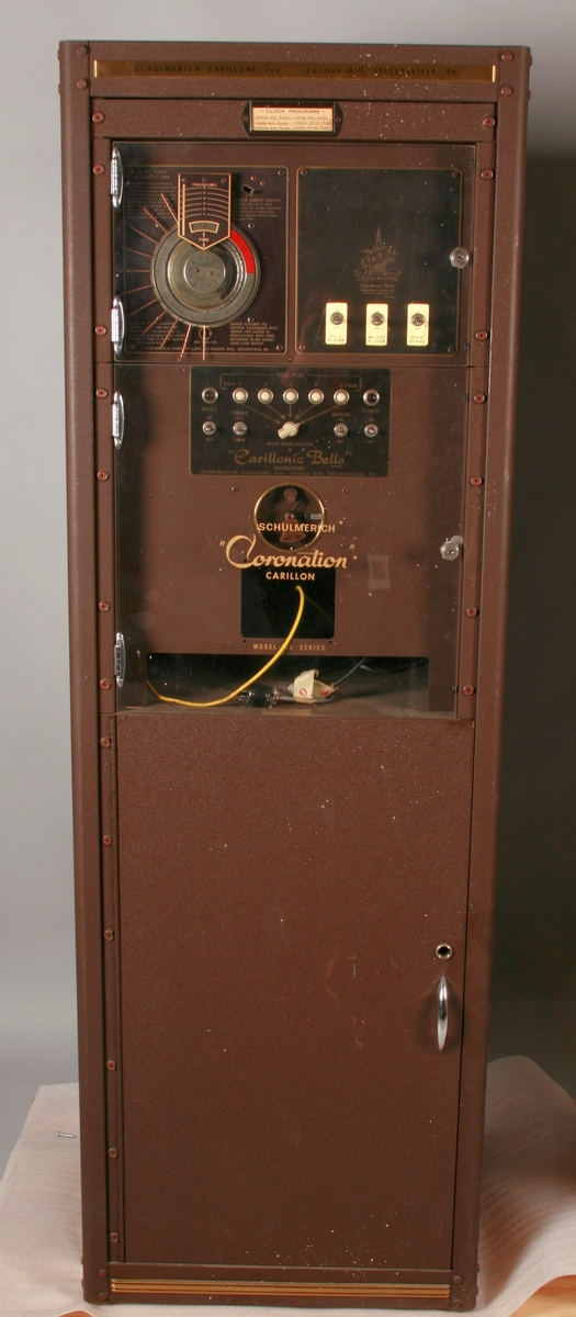 To brunmalte skap i metall (samme størrelse). Flere ventilasjonsrister.

Det ene skapet (A) inneholder avspiller, forsterker, klokkemekanikk, liten høytaler og øvrig elektronikk (noen deler ser ut å mangle). 
Øvre halvdel: bak pleksiglass som kan lukkes er styresentralen med instillinger for ulike klokkeprogrammer:
Til høyre er switch-knapper for å aktivere de tre funksjonene 
a) avspilling av musikkrull 
b) bruk av manuelt spillebord og 
c) timeslag.

Over til venstre er en timer for å skjemalegge de ulike aktivitetene:
1) Hverdag avspilling musikkrull
2) Søndag avspilling musikkrull
3) Hverdag avspilling timeslag
4) Søndag avspilling timeslag
5) Hverdag avspilling manuelt spillebord
6) Søndag avspilling manuelt spillebord

I tillegg er et eget panel for å velge ulike fomer av klokkeringinger ('BELL PEAL').

Nedre halvdel: Musikkrullmekanikk med en mekanisk avleser for musikkrullene ('tracker bar'). 30 spor; én for én tone hver. Papirullen løper over en rekke fjærbelastede(?) L-formet tangenter, en for hvert spor. Når et hull passerer en tangent løftes tangenten oppover og gir i sin tur et signal videre om å aktivere akkurat denne tonen.

Det andre skapet (B) idag tomt, usikker funksjon. Har strømforsyning. Sannsynlig forsterker for bruk av høytalere (C-F) i klokketårnet. Se elektronikk (H). Muligens også oppbevaring av musikkruller med mer.